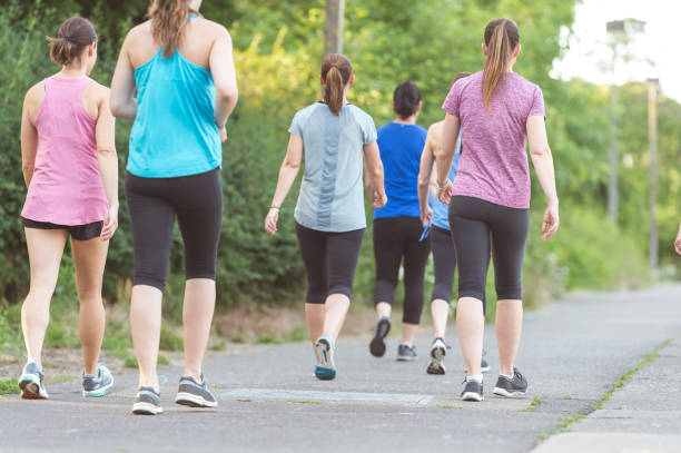 Fundraising Run Group of women participate in a race run/walk to raise money for breast cancer research. They are wearing race bibs and are on a sidewalk, with trees on the left side. The shot is from behind them as they walk along the sidewalk. racewalking stock pictures, royalty-free photos & images