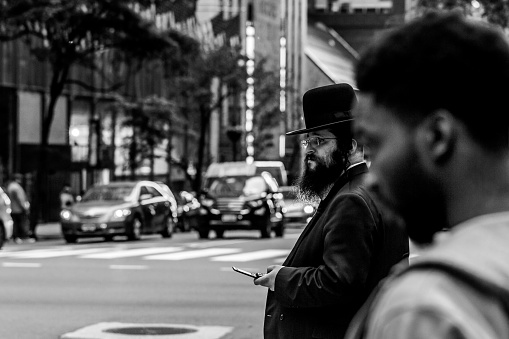 New York, United States - May 30, 2018: Young traditionally dressed hassidic man walks, crossing the street in the opposite direction.