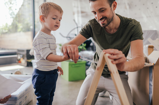 Photo of a young father with his little boy, assembling furniture together after moving into their new home