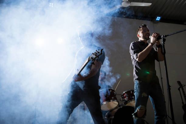 Rock music on stage Rock singer performing on stage with guitarist. Bright light and smoke on stage. rock group photos stock pictures, royalty-free photos & images