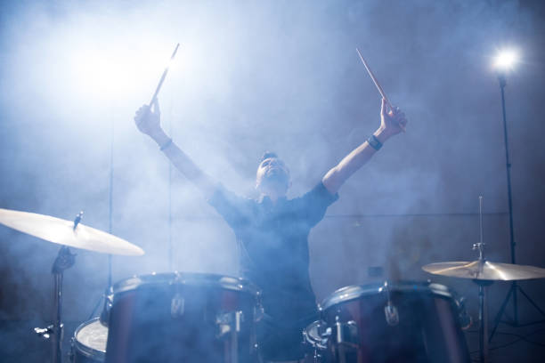 Rock band drummer on stage Rock band drummer raising his arms on stage with light and smoke rock group photos stock pictures, royalty-free photos & images