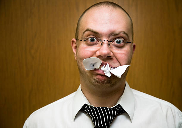 Man with a mouthful of paper and confused facial expression stock photo