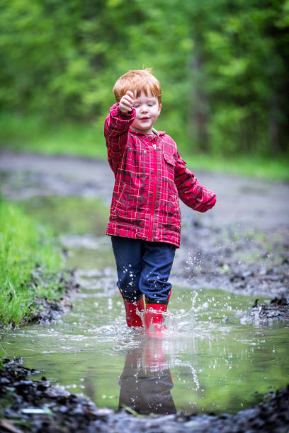 istock Young Cute Kid Walking Jumping into Water Puddle 966679886