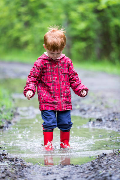 istock Young Cute Kid Walking Jumping into Water Puddle 966682280