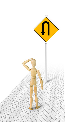 Man in confusion standing in front of Turn Back road sign. Conceptual image with a wooden puppet