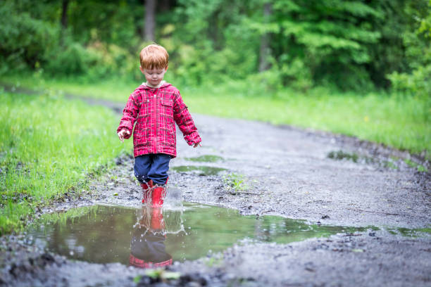 istock Young Cute Kid Walking Jumping into Water Puddle 966692218