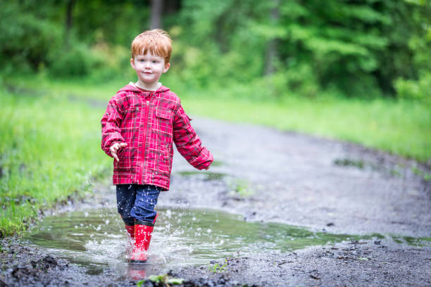 istock Young Cute Kid Walking Jumping into Water Puddle 966692220
