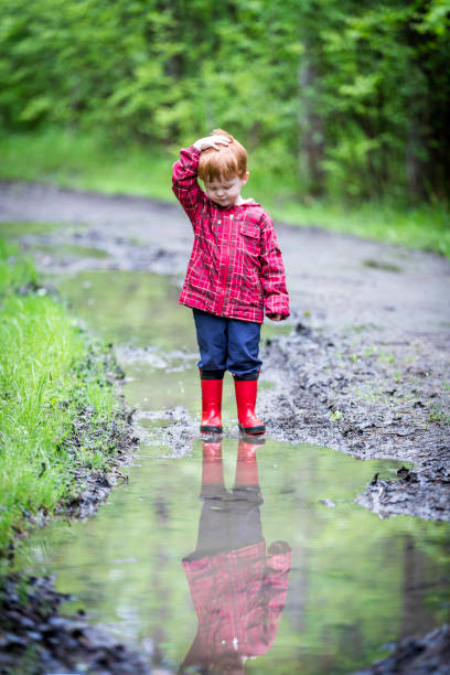 istock Young Cute Kid Walking Jumping into Water Puddle 966692228