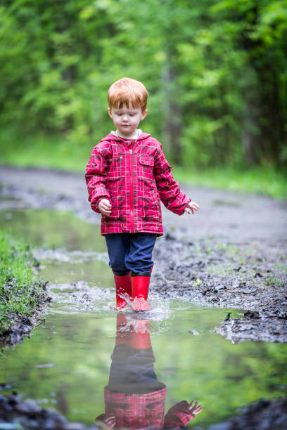 istock Young Cute Kid Walking Jumping into Water Puddle 966692230