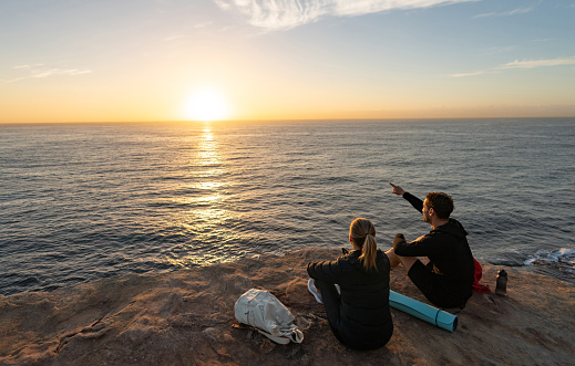 Happy couple hiking and watching a beautiful sunrise at a cliff - outdoors concepts