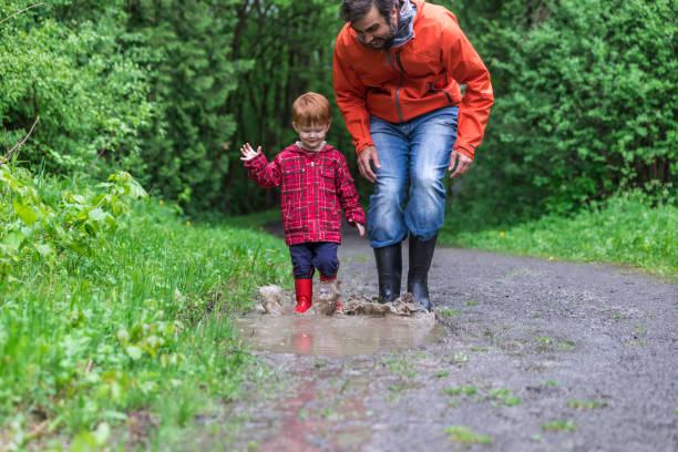istock Young Cute Kid Walking Jumping into Water Puddle with Dad 966709388