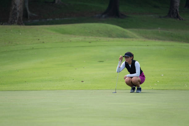 Female golfer lines up her long putt A young Asian woman takes a long putt putting golf stock pictures, royalty-free photos & images