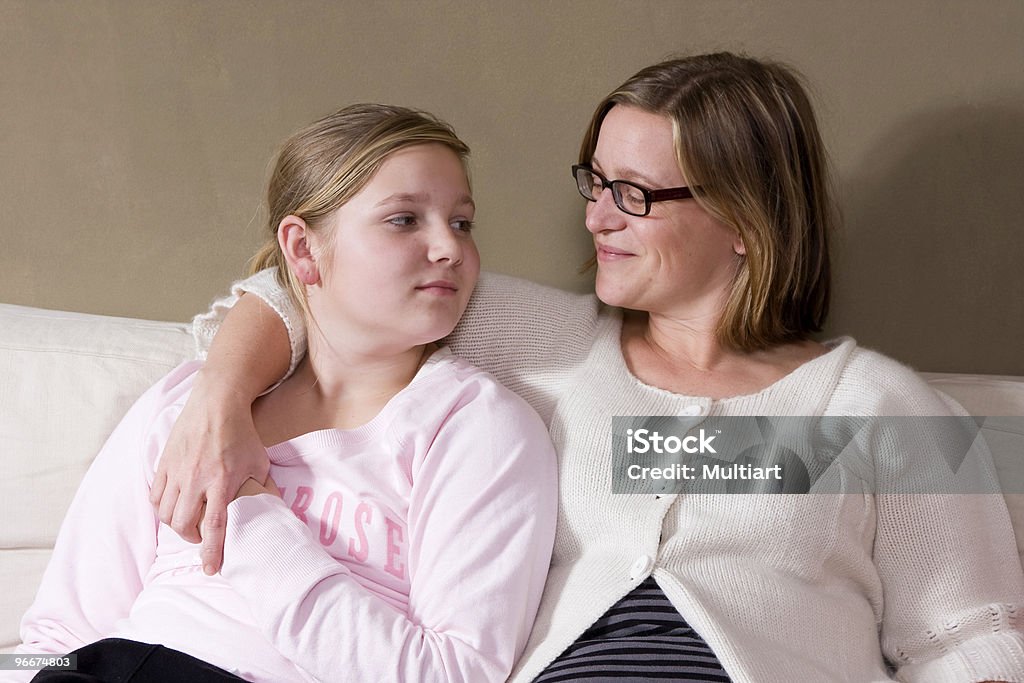 Mother draping arm over daughter in a white couch Mother and daughter having conversation Parent Stock Photo