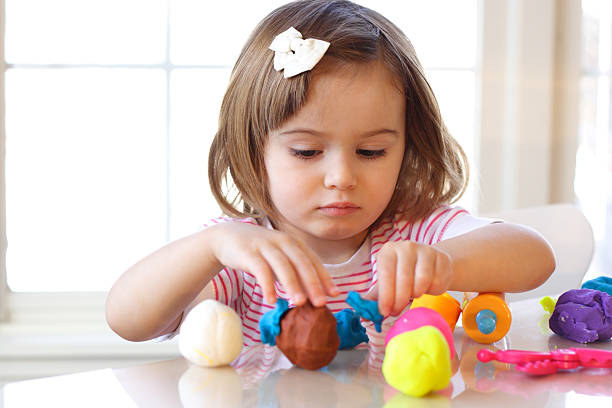 Young girl with bow in hair playing a playdough game stock photo