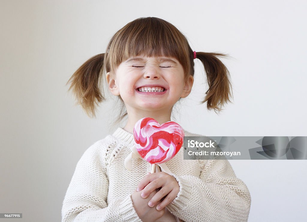 Giddy young girl with a heart-shaped lollipop Beautiful little girl holding a big heart shaped lollipop Child Stock Photo