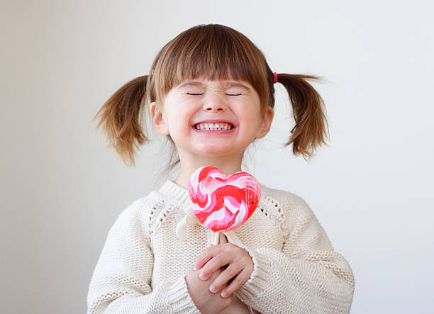 Giddy young girl with a heart-shaped lollipop Beautiful little girl holding a big heart shaped lollipop sugar food photos stock pictures, royalty-free photos & images