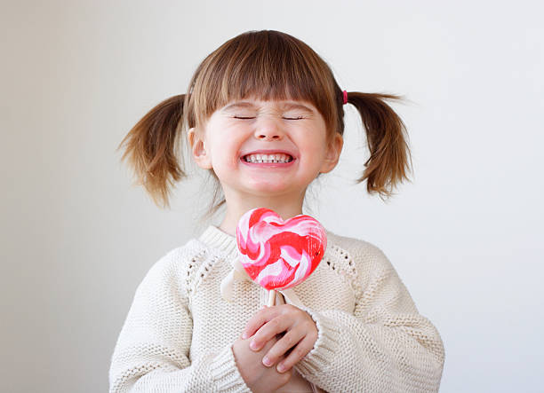 Giddy young girl with a heart-shaped lollipop Beautiful little girl holding a big heart shaped lollipop Pigtails stock pictures, royalty-free photos & images