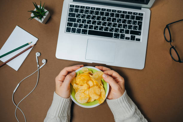 istock Woman hands with chips and laptop on brown background. Top view. Flat lay 966782808