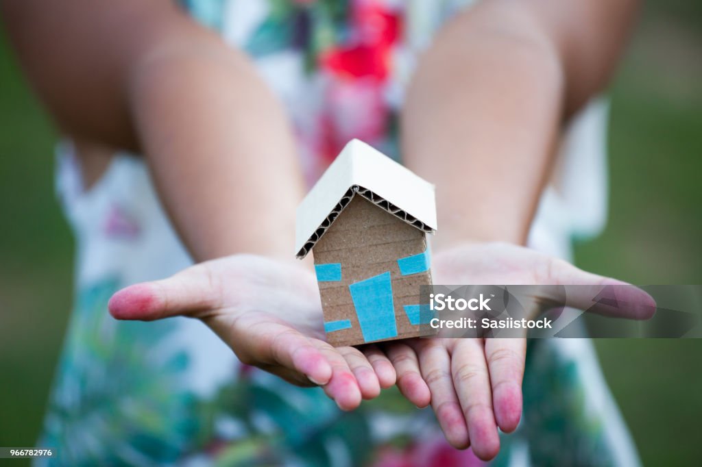 Child holding paper house in hands as real estate and family home concept Homelessness Stock Photo