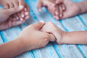 Parent and children holding hands and praying together on blue wooden table