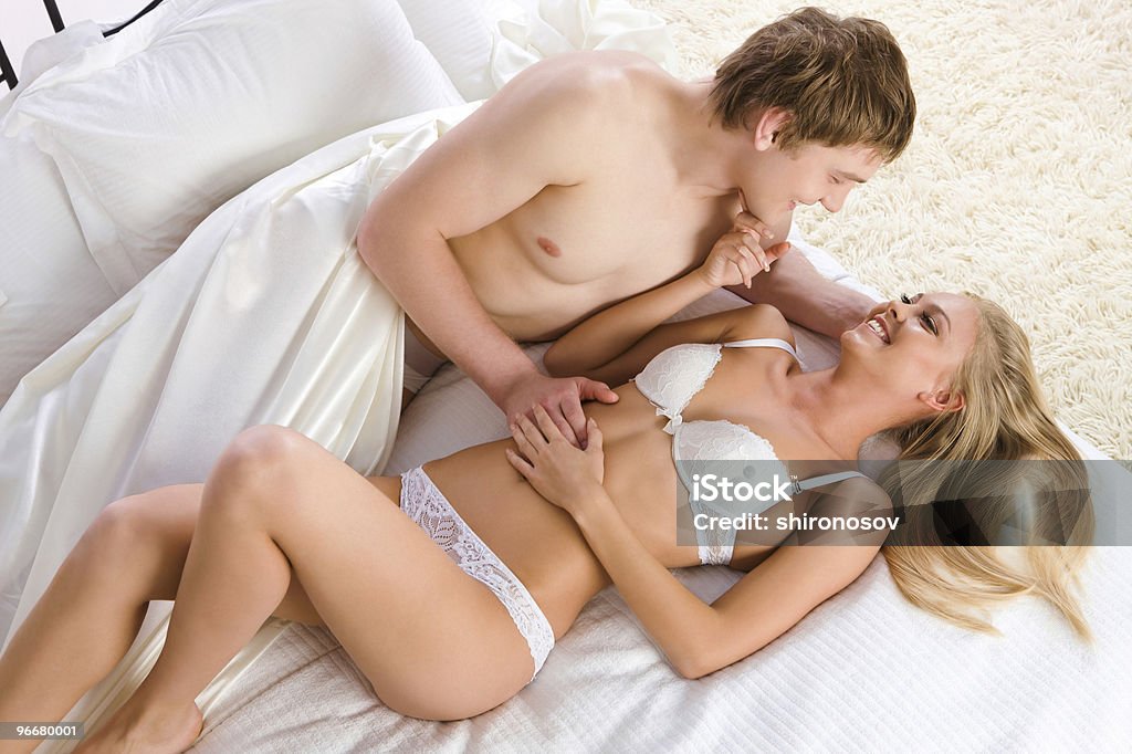 A scantily clad smiling couple laying together on a bed Photo of happy husband and wife lying on bed and looking at each other Adult Stock Photo
