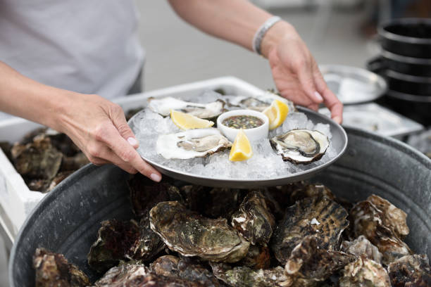 close-up de servidor com bandeja de ostras frescas de concha com fatias de limão, servidas como aperitivo - prepared oysters prepared shellfish shucked seafood - fotografias e filmes do acervo