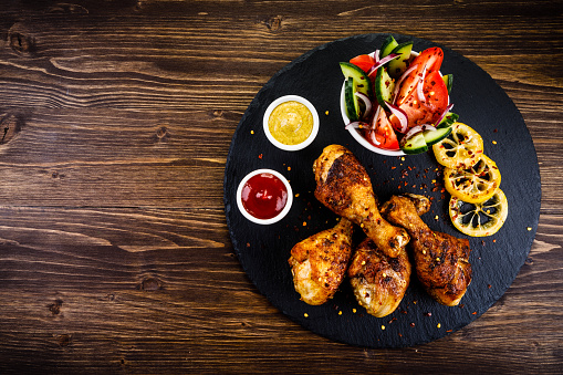 Roast chicken legs with French fries on wooden table