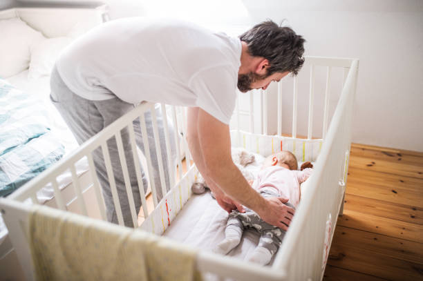 istock Father putting a sleeping toddler girl into cot at home. 966825636