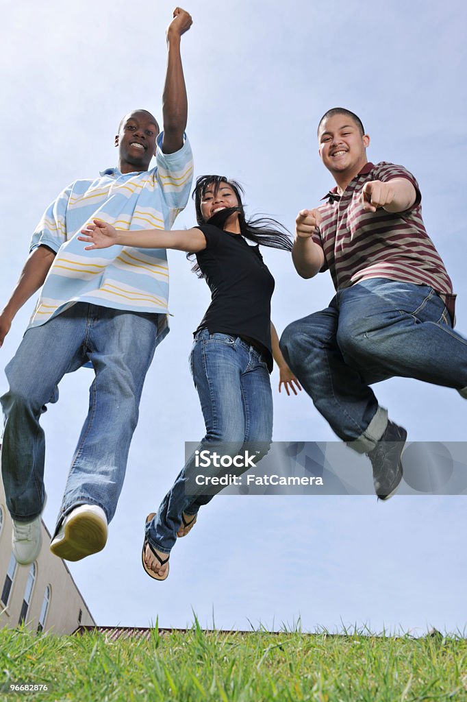 Multi ethnic group of students Three young adults jumping.    High School Stock Photo