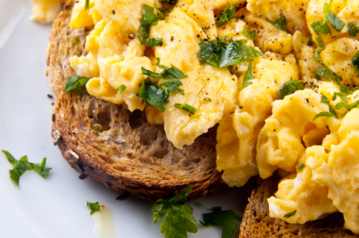 Top-down view of a plate of fluffy and buttery scrambled eggs against a black background