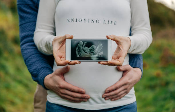 彼女のパートナーは、携帯電話で妊娠を示す超音波 - announcement message 写真 ストックフォトと画像