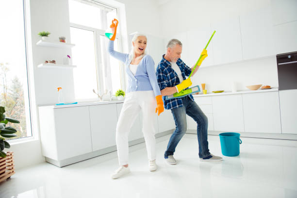 full size, fullbody portrait of crazy foolish funny mad cool couple of senior dancing, singing, man playing on mop like guitar, woman holding spray in raised hand, positive people concept - spring cleaning women cleaning dancing imagens e fotografias de stock