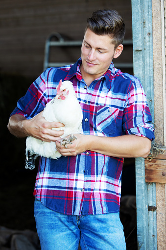 portrait of handsome blond man holding a white chicken