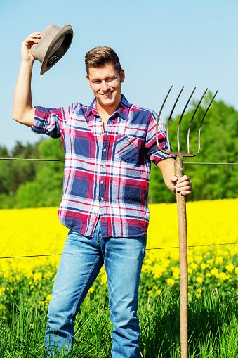 portrait of handsome man with pitchfork standing in front of yellow field