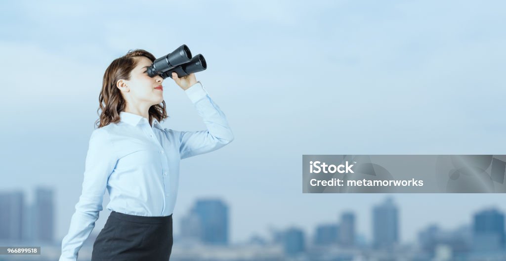 Young businesswoman using binoculars in front of the city. Binoculars Stock Photo
