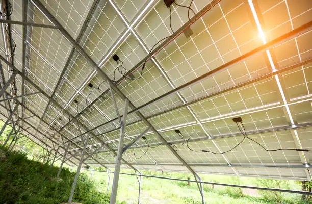 Interior of stand-alone photo voltaic solar system secured on metal rear legs on green grass, lit by summer sun. Alternative energy, environment protection and cheap electricity production concept.