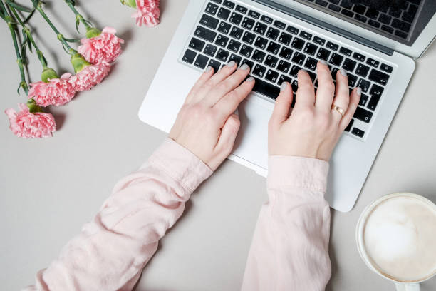 istock Woman hands with coffee and laptop, flowers carnations on white background. spring work space background. Top view 966920946
