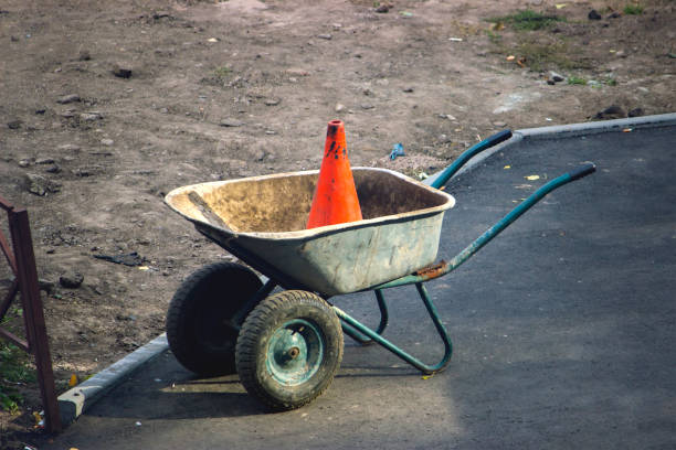 rustic dirty construction wheelbarrow with push broom on the street, orange road construction cone in the background.