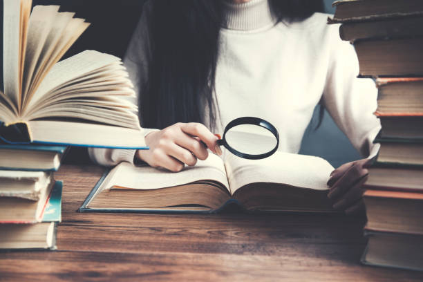istock woman hand  magnifier with books on table 967025724