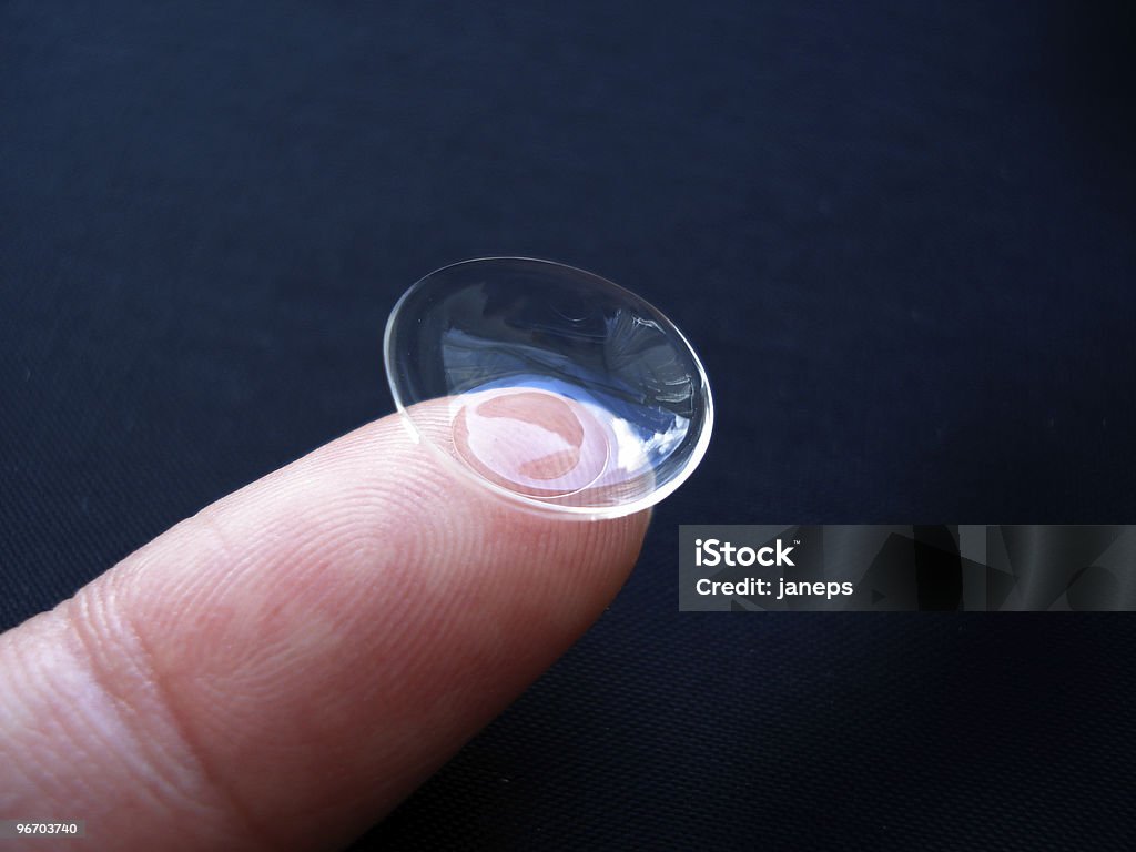 Close-up image of a contact lens resting on a fingertip Contact lens on finger, black background                               Black Color Stock Photo