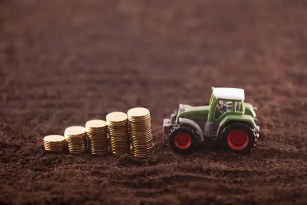 Photo of Tractor miniature with coins on fertile soil land