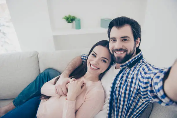 Self portrait of cheerful positive  couple with beaming smiles lying indoor in house, shooting selfie on front camera. True feelings lovestory concept