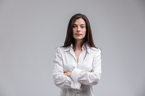 Portrait of long-haired brunette woman wearing white shirt standing with arms crossed