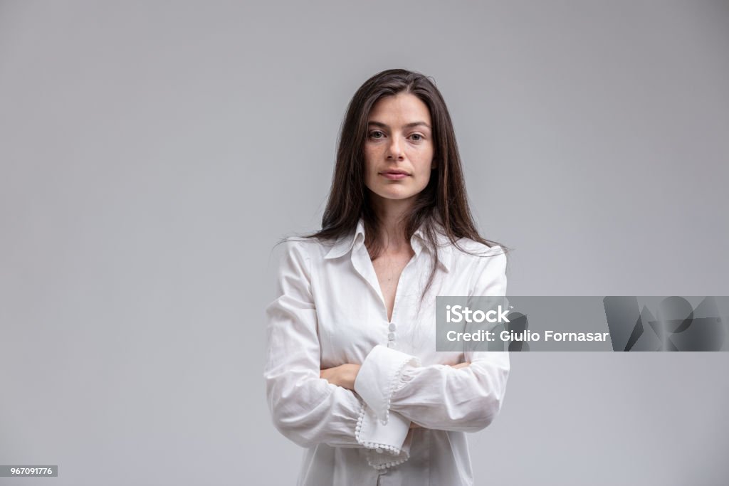 Long-haired woman standing with arms crossed Portrait of long-haired brunette woman wearing white shirt standing with arms crossed Women Stock Photo