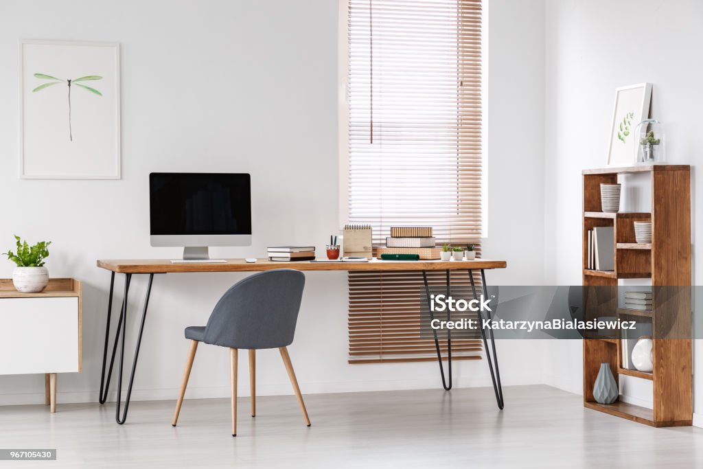 Grey chair at desk with computer monitor in minimal workspace interior with poster. Real photo Grey chair at desk with computer monitor in minimal workspace interior with poster Home Office Stock Photo