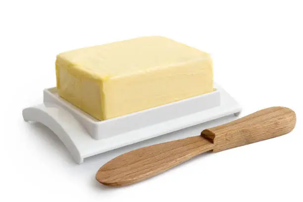 A whole block of butter on white plastic butter dish isolated on white. Wooden butter knife.