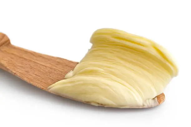 Detail of butter spread on wooden knife on white background.