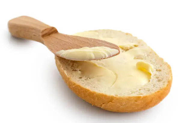 Butter spread on a half of crusty bread roll with a wooden knife isolated on white.