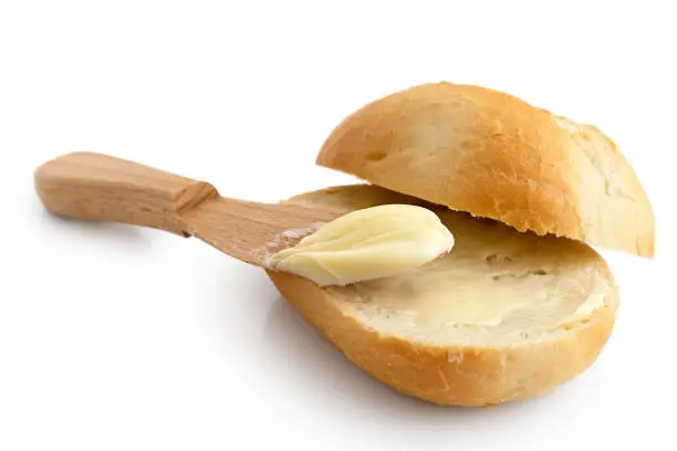 Butter spread on a cut crusty bread roll with a wooden knife isolated on white.