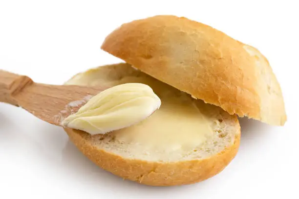 Detail of butter spread on a cut crusty bread roll with a wooden knife isolated on white.